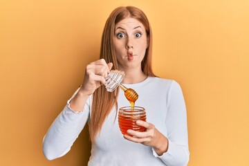 Young irish woman holding honey making fish face with mouth and squinting eyes, crazy and comical.