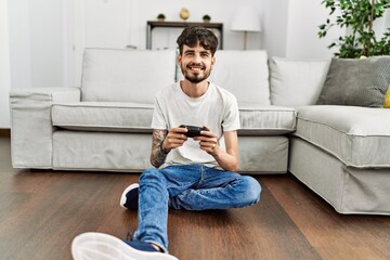 Young hispanic man playing video game sitting on the floor at home.