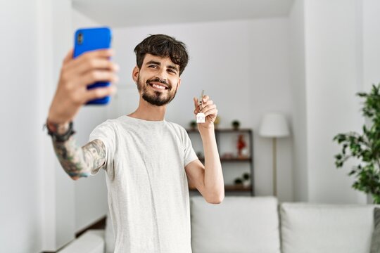 Young hispanic man making selfie by the smartphone holding key of new home