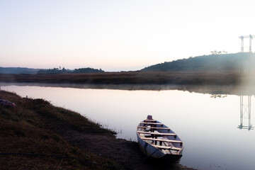 traditional wood boat at calm lake with white mist and flat sky reflection at morning