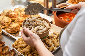 the hand of an unrecognizable person putting chicken wings into a paper box at a food counter,...