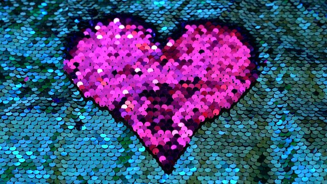 Pink beating heart on a T-shirt decorated with sequins. Pink on turquoise. Shiny circles in the form of a pink heart on a blue background. A pulsating heart made of sequins.