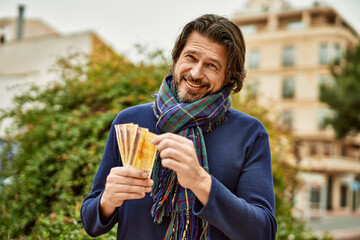 Middle age handsome man holding norwegian krone banknotes outdoors at the park