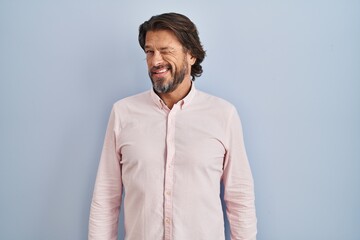 Handsome middle age man wearing elegant shirt background winking looking at the camera with sexy expression, cheerful and happy face.