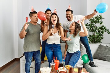 Group of young hispanic friends having birthday party singing song using microphone at home.