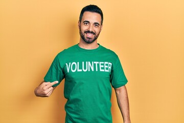 Handsome hispanic man with beard wearing volunteer t shirt smiling happy pointing with hand and finger