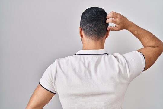 Young hispanic man with beard wearing casual clothes over white background backwards thinking about doubt with hand on head