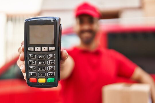 Young hispanic man courier holding package and data phone at street