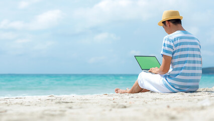 Lifestyle young asian man working on laptop while sitting chill on the beautiful outdoor beach, freelance working social on holiday summer. Summer and Vacation Concept