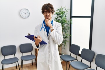 Young hispanic doctor man at waiting room thinking worried about a question, concerned and nervous...
