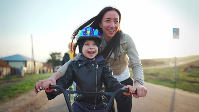 Childhood bike concept. Mother teaching son to ride bicycle. Young mom teaching son to ride bike first time on countryside rural road at sunset. Happy kids on bikes. The best moments together.