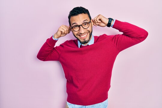 Hispanic man with beard wearing business shirt and glasses smiling pulling ears with fingers, funny gesture. audition problem
