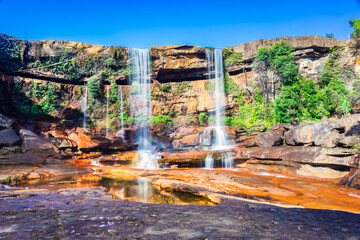 waterfall falling from mountain top with reflection and blue sky at morning from low angle