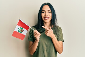 Young hispanic girl holding peru flag smiling happy pointing with hand and finger