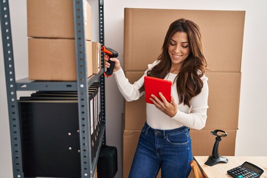 Young hispanic woman ecommerce business worker scanning package using barcode reader at office