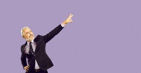 Overjoyed mature man in suit isolated pink studio background dancing having fun. Smiling old businessman in formalwear make funny dancer movements. Victory gesture. Copy space.