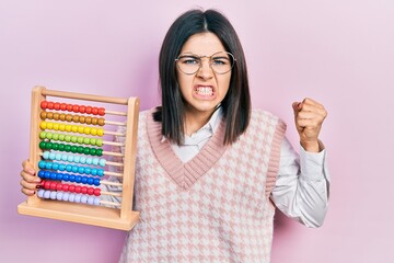 Young brunette woman holding traditional abacus annoyed and frustrated shouting with anger, yelling...