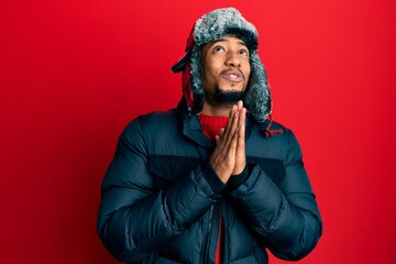Young african american man with beard wearing winter hat and coat begging and praying with hands...