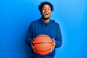Young african american man with beard holding basketball ball smiling and laughing hard out loud because funny crazy joke.