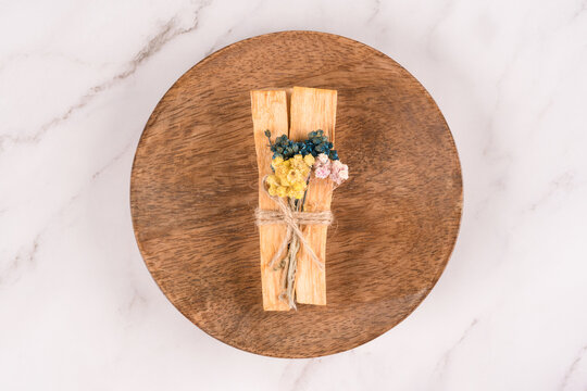 Holy wood sticks with dried flowers bouquet for meditation and spiritual practices, wooden tray with palo santo sticks on white marble table background. Top view