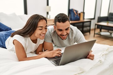 Fototapeta premium Young latin couple smiling happy using laptop at bedroom
