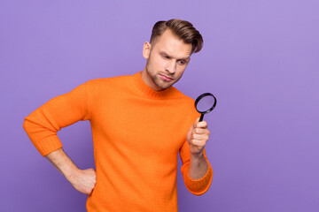 Photo of ponder unsure guy dressed orange pullover looking magnifier empty space isolated purple...