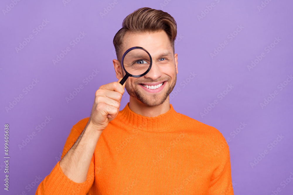 Wall mural photo of cheerful pretty guy wear orange sweater looking researching loupe isolated violet color bac