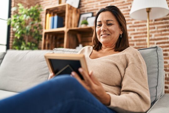 Middle age hispanic woman smiling confident looking picture at home