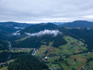 Fototapeta premium Green slopes of Ukrainian Carpathian mountains in summer. Cloudy morning, low clouds. Aerial drone view.