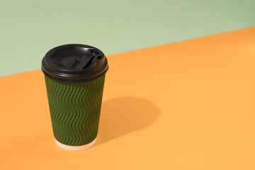 Green eco paper coffee cup on orange and green background with copy space, mockup. Sustainable food packaging concept