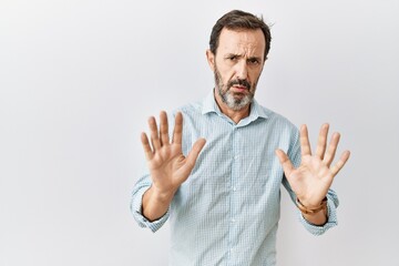 Naklejka premium Middle age hispanic man with beard standing over isolated background moving away hands palms showing refusal and denial with afraid and disgusting expression. stop and forbidden.