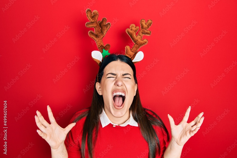 Sticker young hispanic woman wearing cute christmas reindeer horns crazy and mad shouting and yelling with a