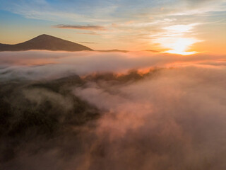 The rays of dawn over the fog in the Ukrainian Carpathians. Aerial drone view.