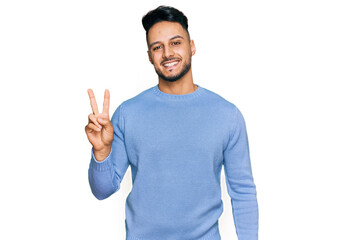 Young arab man wearing casual clothes smiling with happy face winking at the camera doing victory...