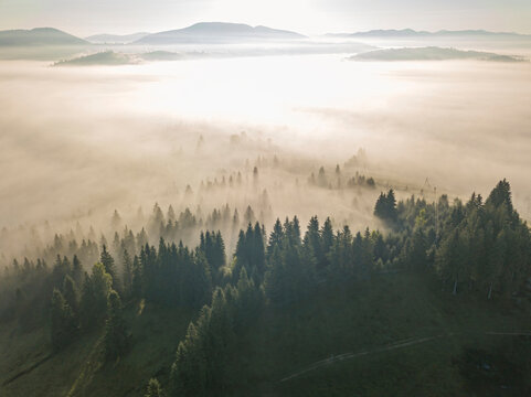 The rays of the morning sun through the fog in the mountains. Aerial drone view. © Sergey