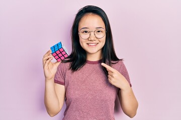 Young chinese girl playing colorful puzzle cube intelligence game smiling happy pointing with hand and finger