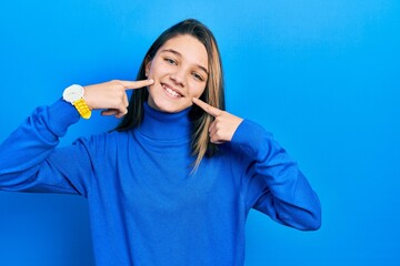 Young brunette girl wearing turtleneck sweater smiling cheerful showing and pointing with fingers teeth and mouth. dental health concept.