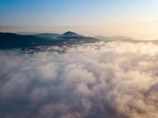 Flight over fog in Ukrainian Carpathians in summer. Mountains on the horizon. Aerial drone view.