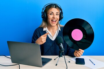 Young caucasian woman working at radio studio holding vinyl disc smiling happy pointing with hand and finger