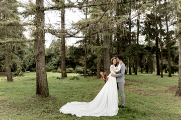 A couple of newlyweds hugging against the backdrop of a green forest