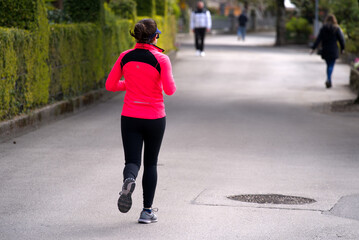Rear view of woman jogging alongside the waterfront of Montreux, Canton Vaud, on a blue cloudy...