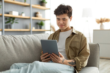 Smiling asian man using digital tablet sitting on couch