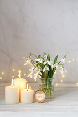 snowdrops flowers, hear decor and candles on table, blurred abstract background. spring season....