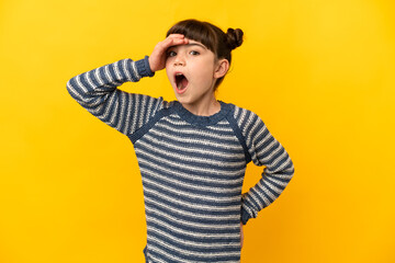 Little caucasian girl isolated on yellow background doing surprise gesture while looking front