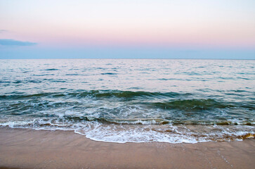Summer evening at the seashore. View of the soft sea wave on the sandy beach.