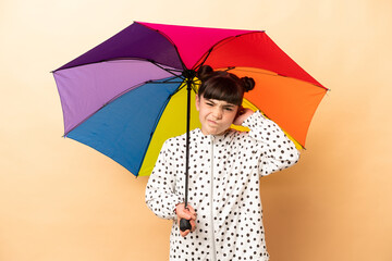 Little girl holding an umbrella isolated on beige background having doubts