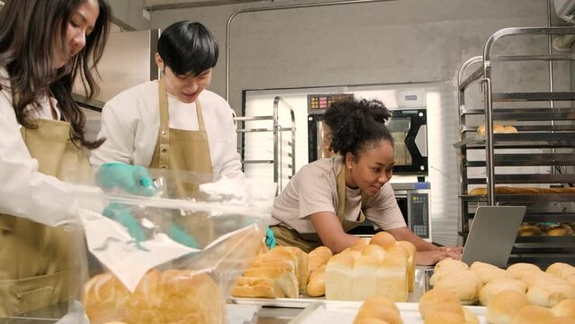 Three young friends and startup partners of bread dough and pastry foods busy with homemade baking jobs while cooking orders online, packing, and delivering on bakery shop, small business entrepreneur