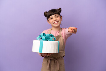 Pastry little girl holding a big cake isolated on purple background pointing front with happy expression