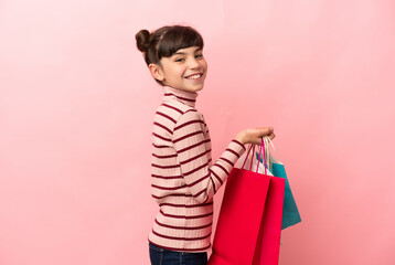 Little caucasian girl isolated on pink background holding shopping bags and smiling