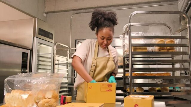 Bakery startup small business delivery. One African American female cook is packing handmade and fresh-baked bread and pastries in boxes and sending for online customer purchases in culinary kitchen.